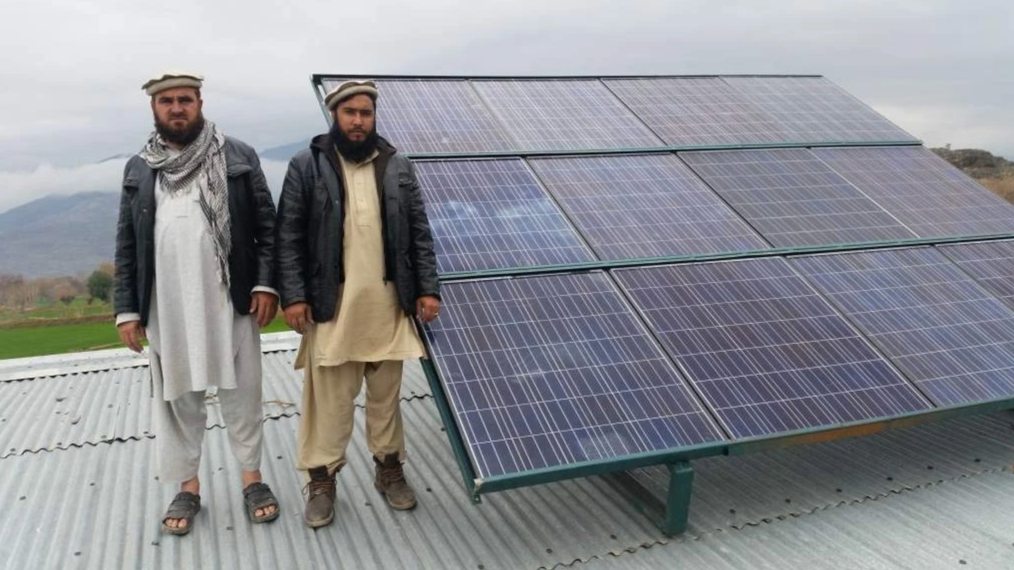 Two community members with completed solar array on school roof